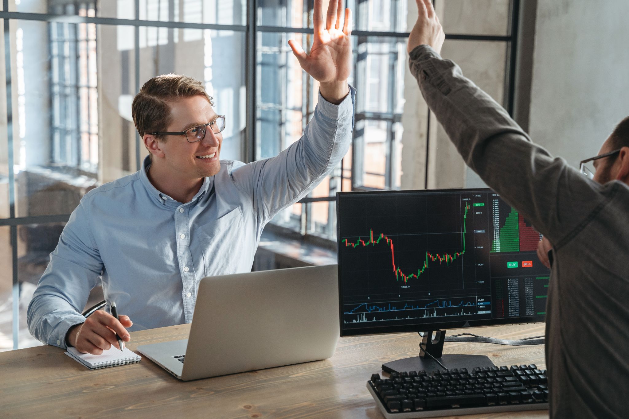 Dos traders celebrando una operación exitosa con un gráfico financiero en pantalla